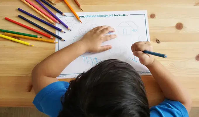 Child at a desk coloring with pencils.
